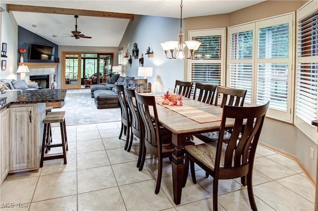 dining room with light tile patterned flooring, lofted ceiling, a tiled fireplace, and ceiling fan with notable chandelier