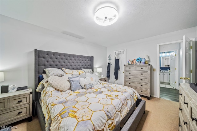 bedroom with light colored carpet, a textured ceiling, and ensuite bathroom