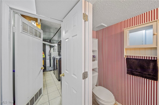 bathroom featuring toilet, washer / clothes dryer, tile patterned flooring, and a textured ceiling