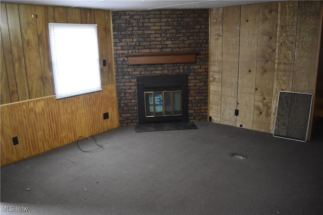 unfurnished living room featuring carpet flooring, wooden walls, and a fireplace