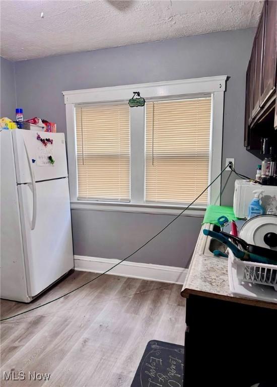 kitchen featuring dark brown cabinetry, a textured ceiling, white fridge, and light wood-type flooring