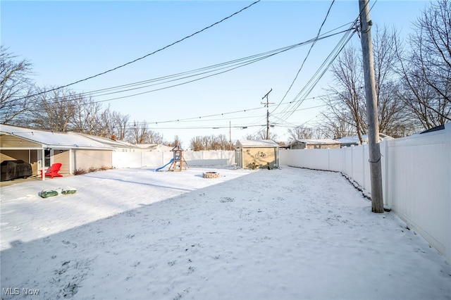 yard covered in snow featuring a playground and a shed