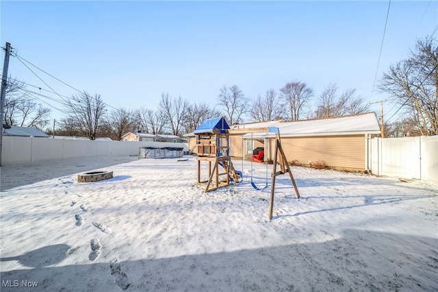 yard covered in snow with a playground and an outdoor fire pit