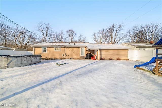 snow covered back of property featuring a playground and a covered pool