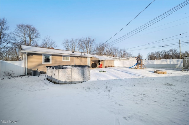 snow covered back of property with a playground and a covered pool