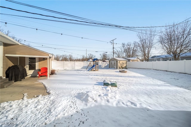 snowy yard with a storage shed and a playground