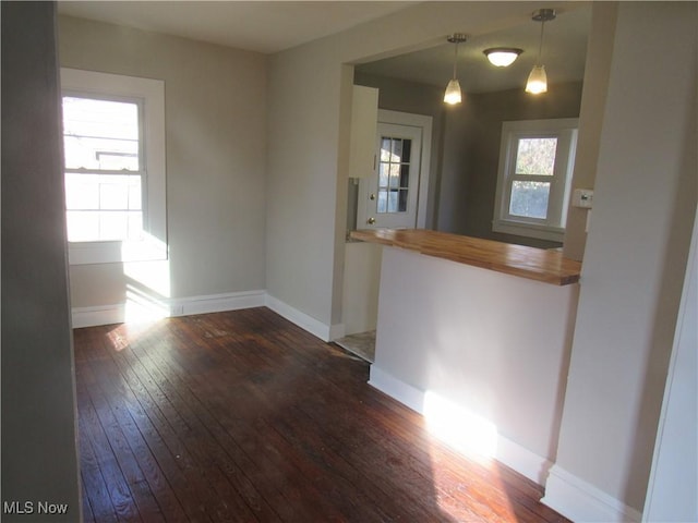 kitchen with dark wood-type flooring, wood counters, hanging light fixtures, and a wealth of natural light