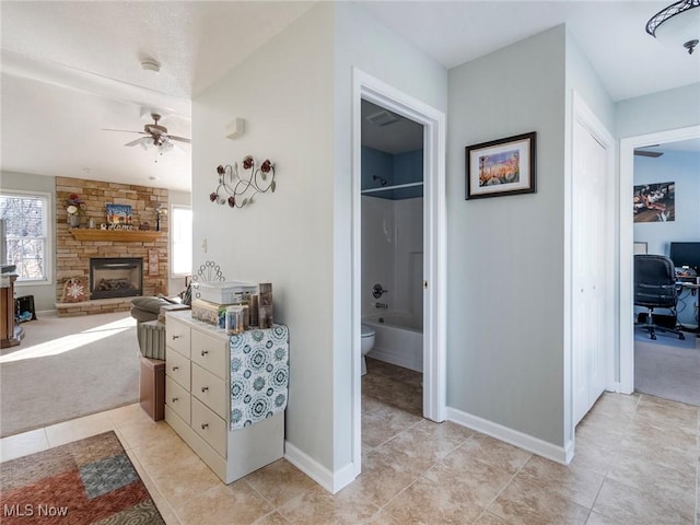 bathroom featuring ceiling fan, toilet, a stone fireplace, and a wealth of natural light