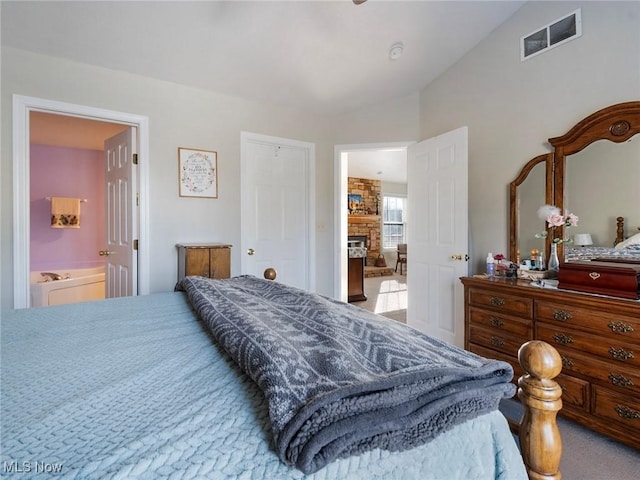 carpeted bedroom with ensuite bathroom, a fireplace, and vaulted ceiling