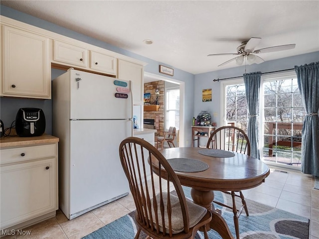 dining space with a stone fireplace, a healthy amount of sunlight, light tile patterned floors, and ceiling fan