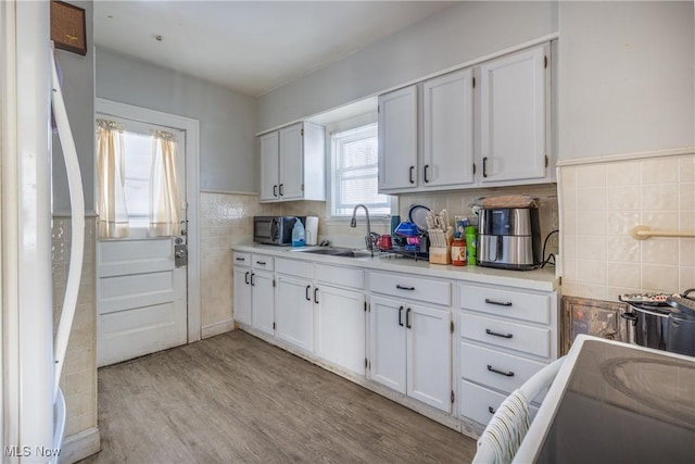 kitchen featuring sink, light hardwood / wood-style flooring, white cabinetry, tile walls, and white refrigerator