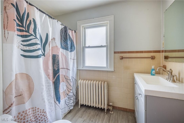 bathroom featuring radiator heating unit, wood-type flooring, tile walls, and vanity