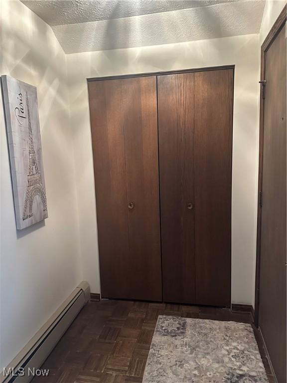 hallway featuring dark parquet flooring, a baseboard heating unit, and a textured ceiling