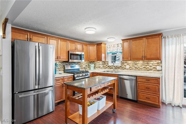 kitchen featuring sink, stainless steel appliances, tasteful backsplash, light stone countertops, and dark hardwood / wood-style flooring