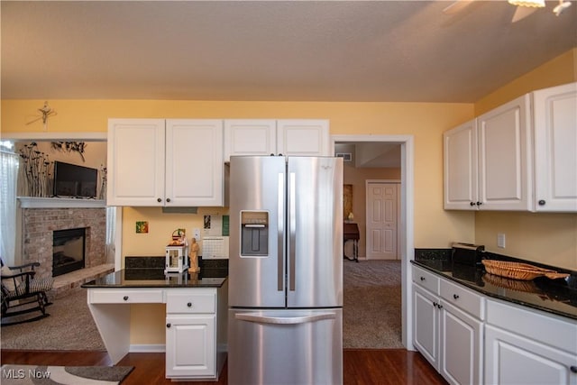 kitchen featuring a fireplace, dark stone countertops, stainless steel fridge, and white cabinets