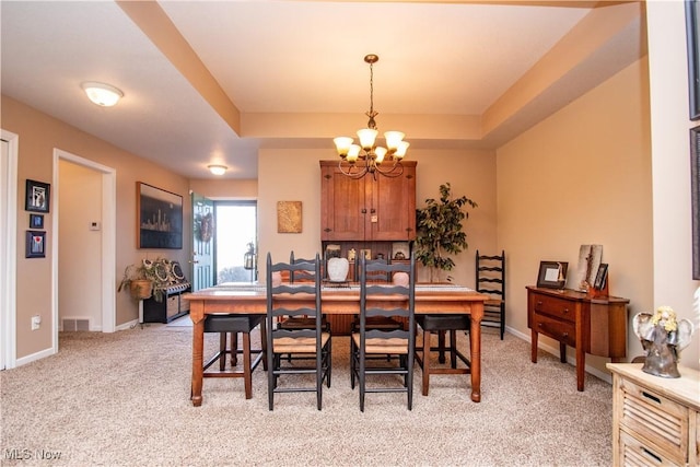 carpeted dining room featuring an inviting chandelier and a raised ceiling