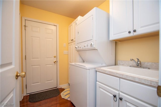 clothes washing area with stacked washer / drying machine, sink, dark wood-type flooring, and cabinets