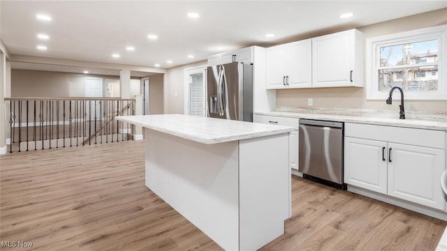 kitchen with light stone counters, a center island, light hardwood / wood-style flooring, appliances with stainless steel finishes, and white cabinets