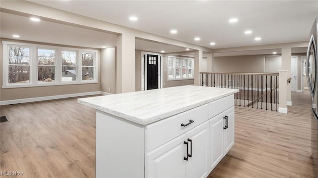 kitchen with light hardwood / wood-style floors, light stone countertops, a center island, and white cabinets