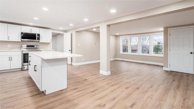 kitchen with white cabinetry, a center island, light wood-type flooring, stainless steel appliances, and light stone countertops