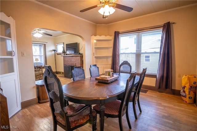 dining area featuring light hardwood / wood-style flooring, a fireplace, ornamental molding, and ceiling fan