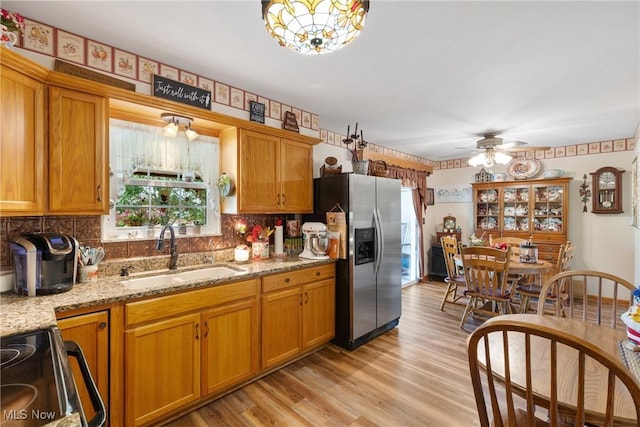 kitchen with appliances with stainless steel finishes, sink, backsplash, light stone counters, and light hardwood / wood-style floors