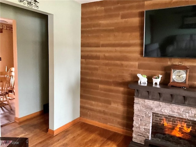 unfurnished living room featuring wood-type flooring, a stone fireplace, and wood walls