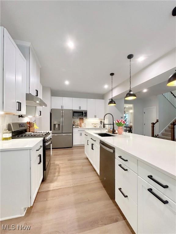 kitchen featuring under cabinet range hood, light wood-style flooring, appliances with stainless steel finishes, white cabinets, and a sink