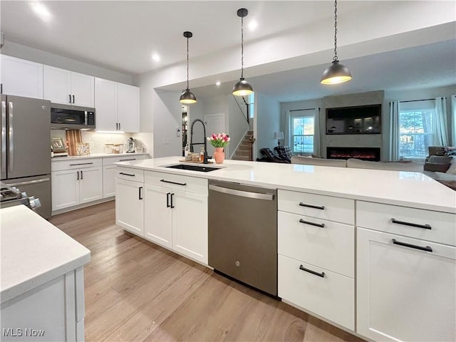 kitchen with light wood-style flooring, a sink, open floor plan, appliances with stainless steel finishes, and light countertops