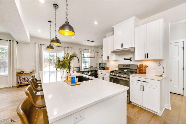 kitchen with light wood finished floors, under cabinet range hood, stainless steel range with gas stovetop, light countertops, and a sink