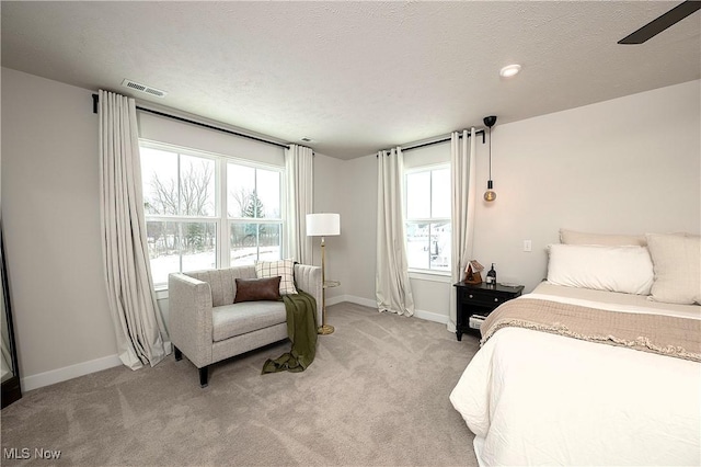 bedroom with a textured ceiling, light colored carpet, visible vents, and baseboards