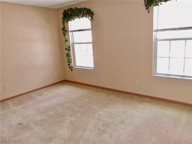 spare room featuring light carpet and baseboards