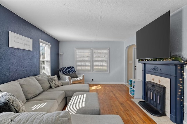 living room with a tiled fireplace, a textured ceiling, and light hardwood / wood-style flooring