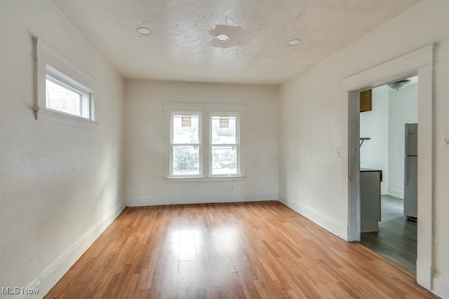 empty room with a textured ceiling and light hardwood / wood-style flooring