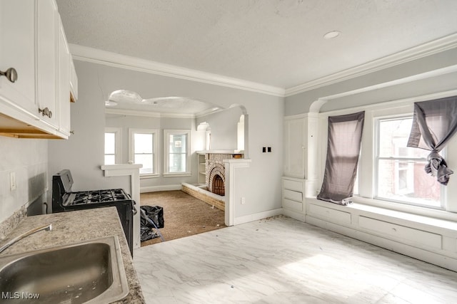 kitchen with gas stove, sink, crown molding, light stone countertops, and white cabinets