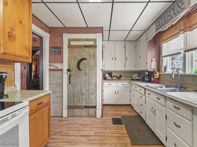 kitchen featuring white electric range, sink, light hardwood / wood-style flooring, white cabinets, and a drop ceiling