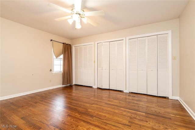 unfurnished bedroom with ceiling fan, dark wood-type flooring, and multiple closets