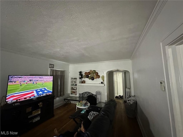 living room with dark wood-type flooring, crown molding, a brick fireplace, and a textured ceiling