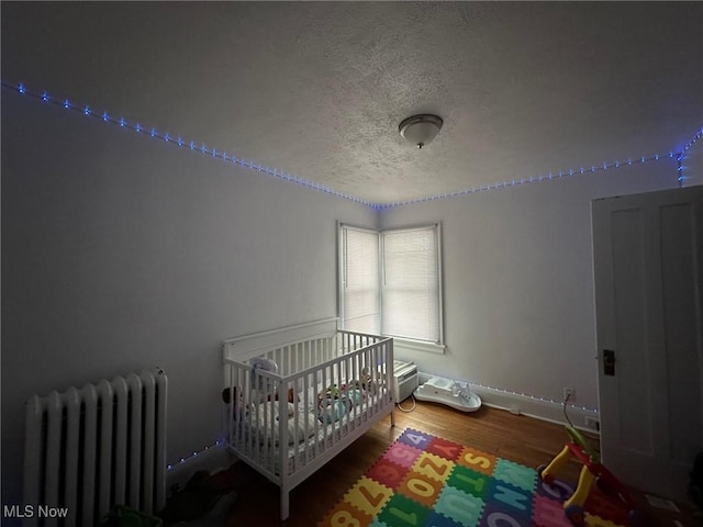 bedroom with hardwood / wood-style flooring, radiator, a crib, and a textured ceiling