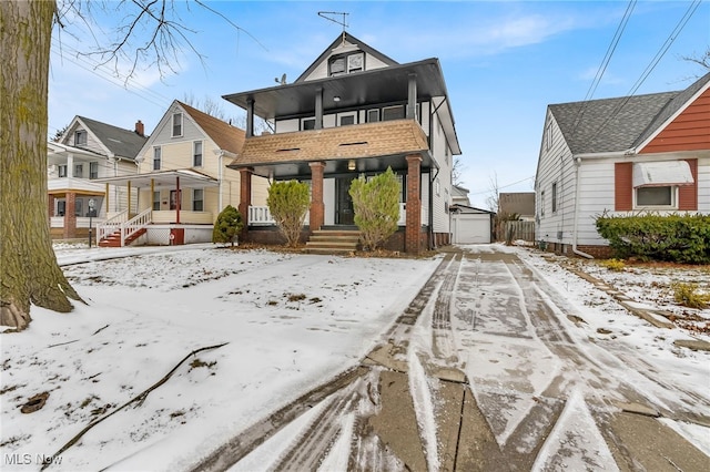 snow covered rear of property with a porch, a garage, and an outbuilding