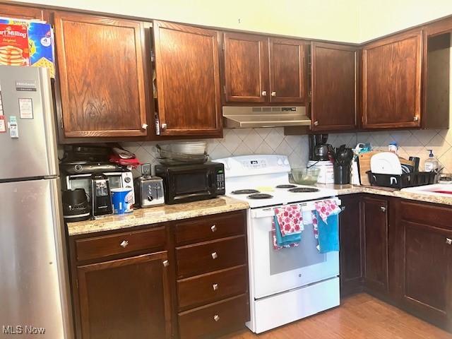 kitchen with white electric range, light stone counters, tasteful backsplash, stainless steel refrigerator, and light hardwood / wood-style floors