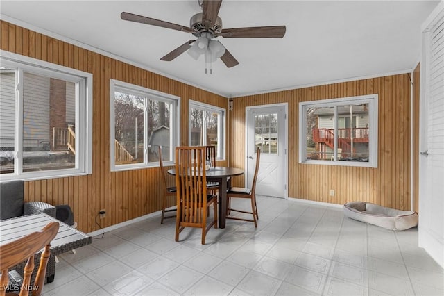 dining room with ceiling fan, ornamental molding, and wood walls