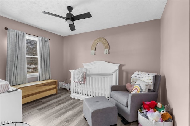 bedroom featuring a crib, wood-type flooring, a textured ceiling, and ceiling fan