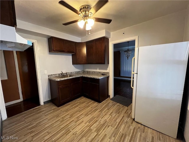 kitchen with sink, light stone counters, dark brown cabinets, white refrigerator, and ceiling fan