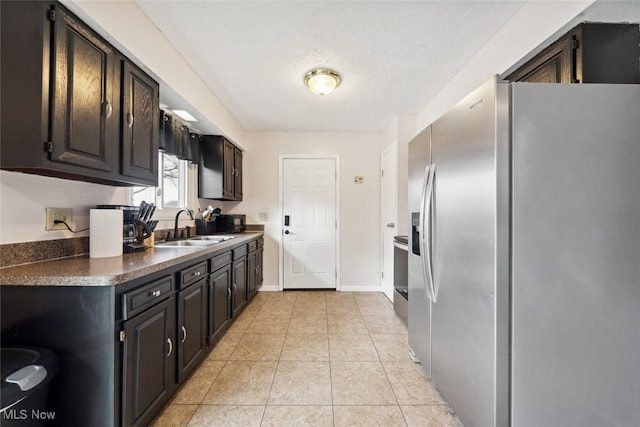 kitchen featuring sink, dark brown cabinetry, a textured ceiling, light tile patterned flooring, and stainless steel fridge with ice dispenser