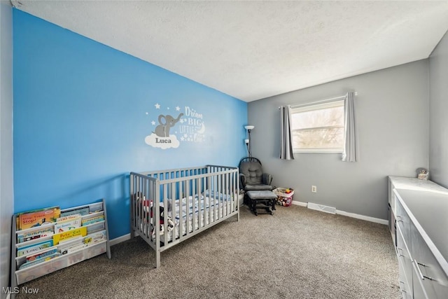 bedroom featuring carpet floors, a nursery area, and a textured ceiling