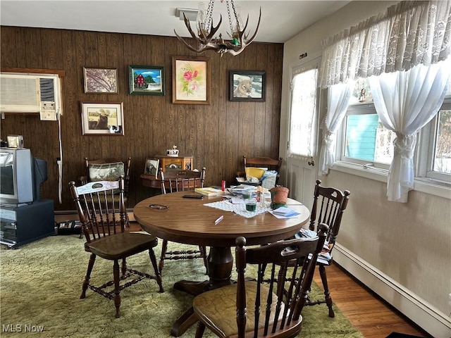 dining area featuring a baseboard heating unit, wooden walls, wood-type flooring, an AC wall unit, and a chandelier