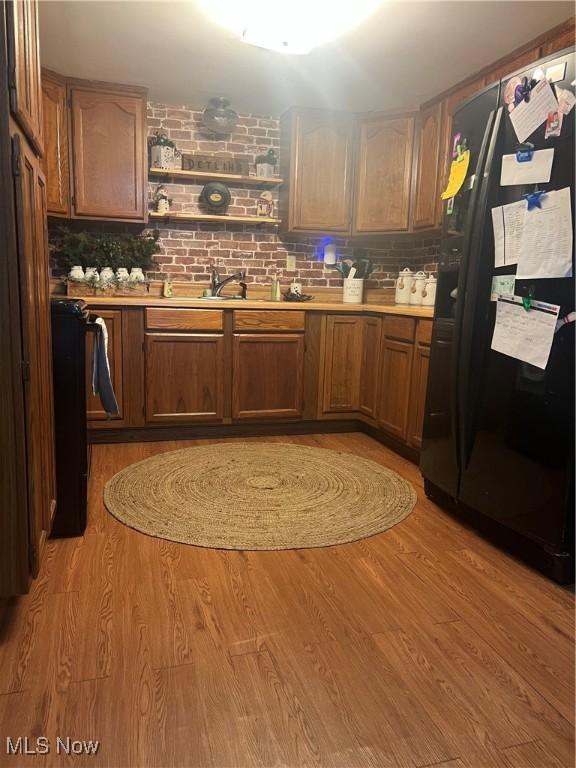 kitchen with sink, black fridge with ice dispenser, light hardwood / wood-style flooring, and backsplash