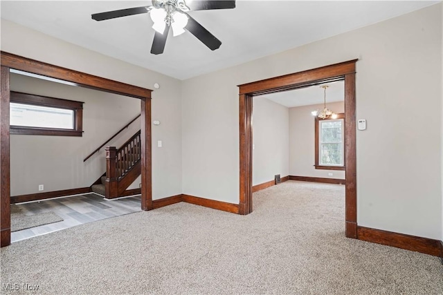 empty room featuring a healthy amount of sunlight, ceiling fan with notable chandelier, and carpet