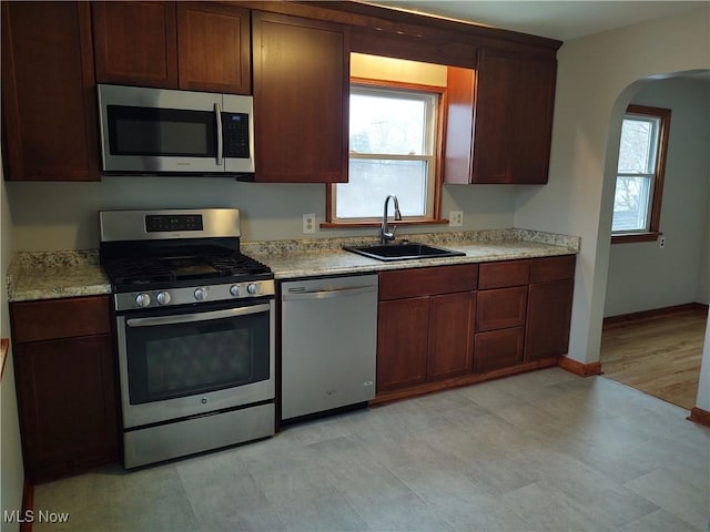 kitchen with appliances with stainless steel finishes, sink, a wealth of natural light, and light stone counters